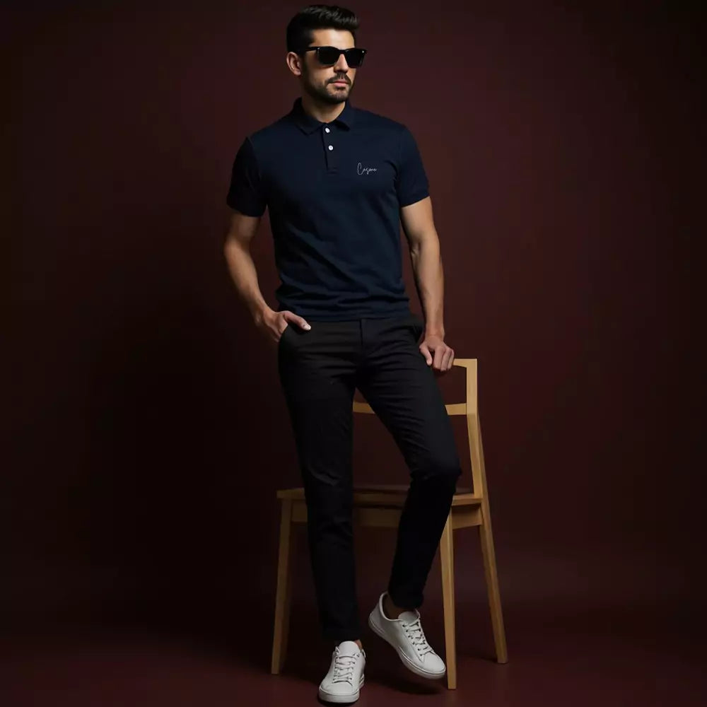 Man wearing a navy polo shirt with a logo, black pants, and white sneakers on a dark background