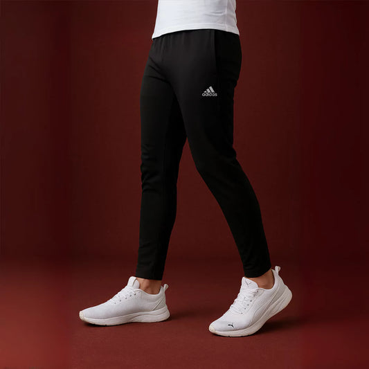 Person wearing black stride pants and white sneakers on a dark red background