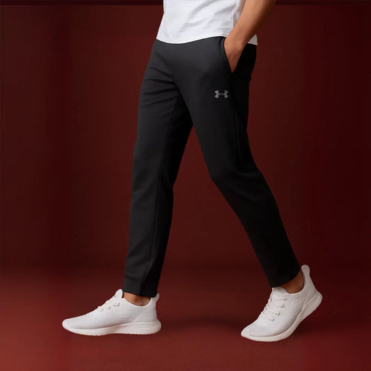 Person wearing black Armour pants and white sneakers on a dark red background