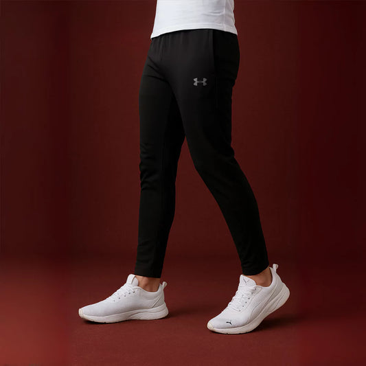 Person wearing black Armour pants and white sneakers on a dark red background