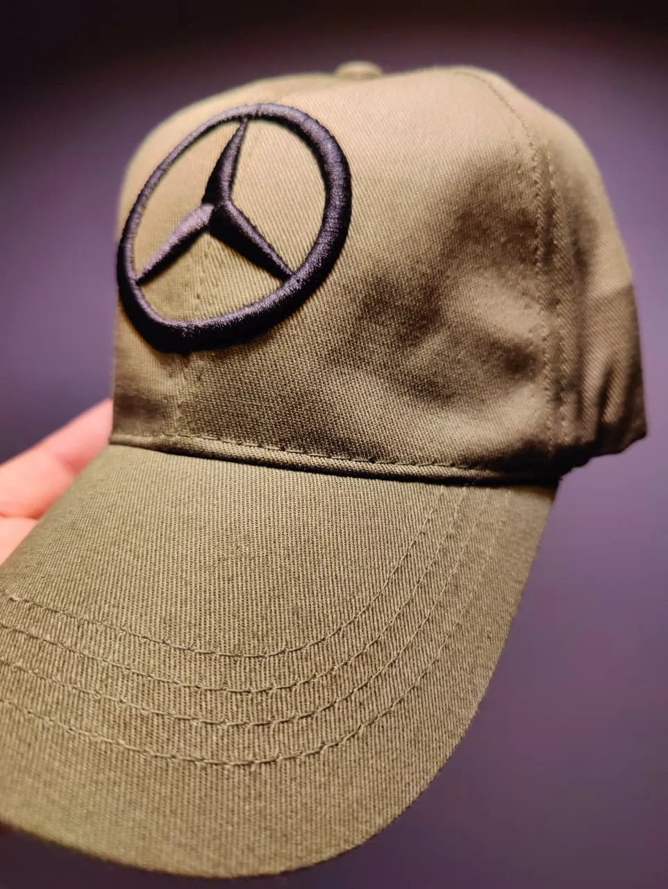 Green cap with Mercedes-Benz logo held against a dark background