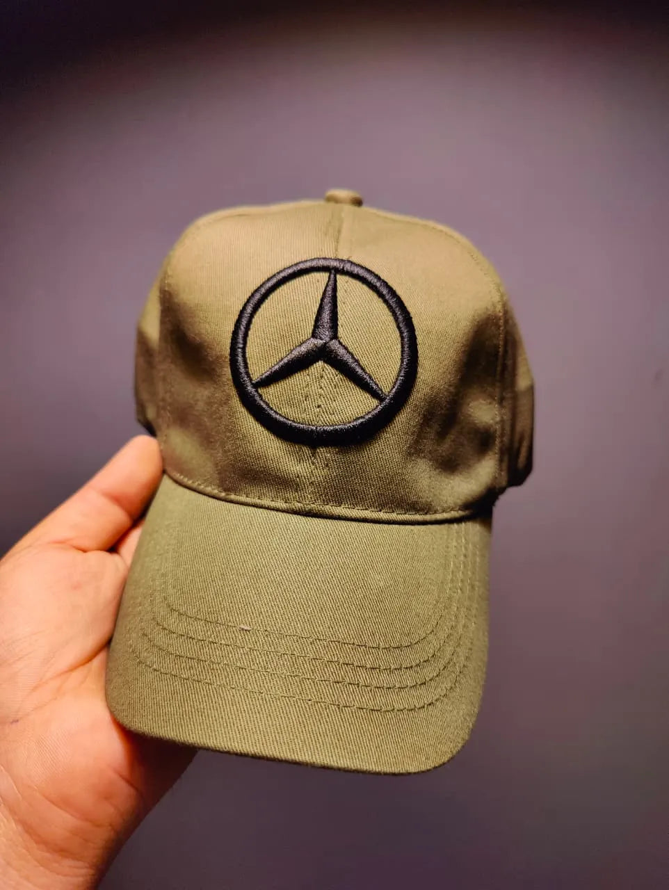 Olive green cap with Mercedes-Benz logo held against a dark background