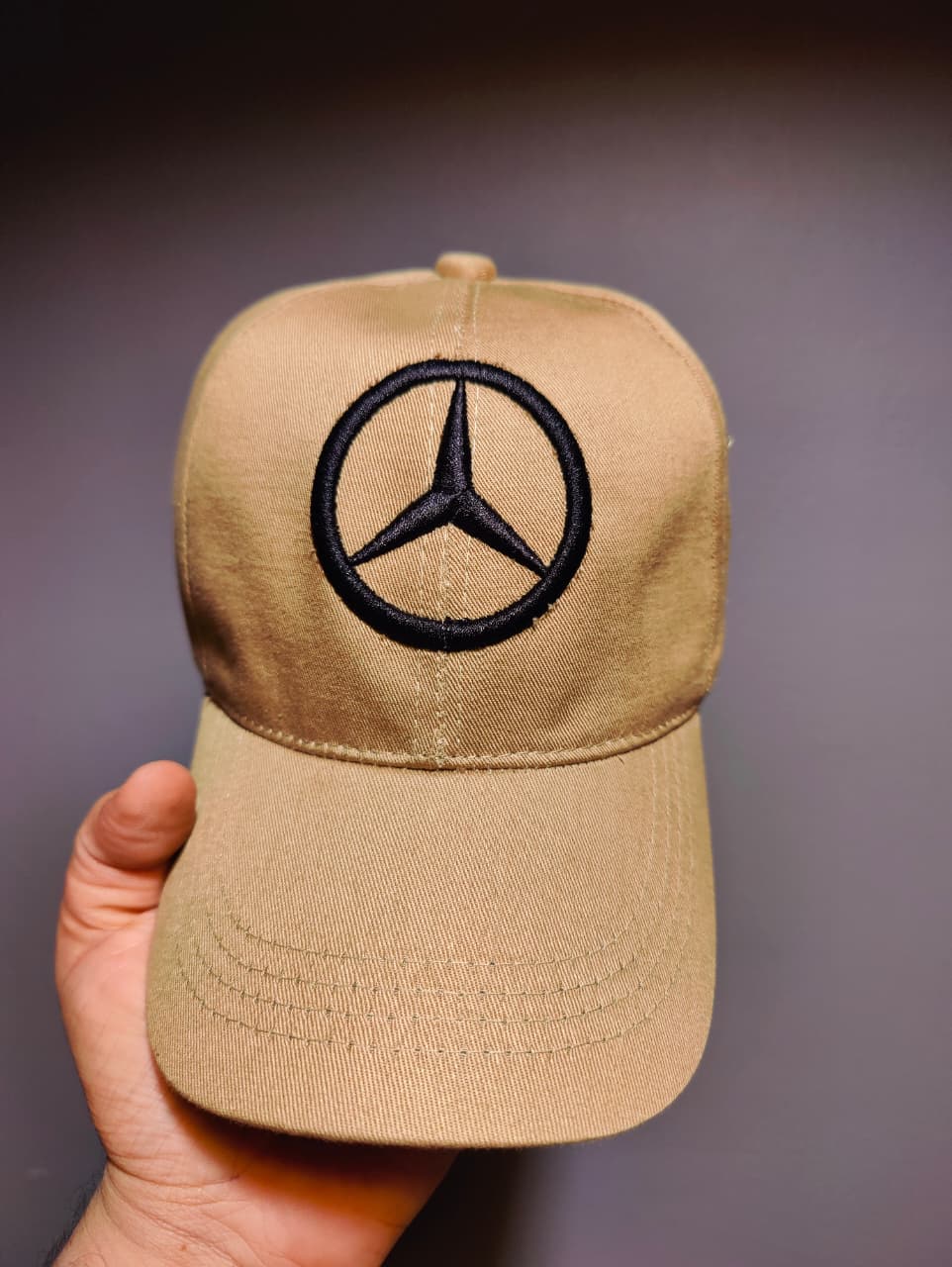 Beige cap with Mercedes-Benz logo held against a dark background
