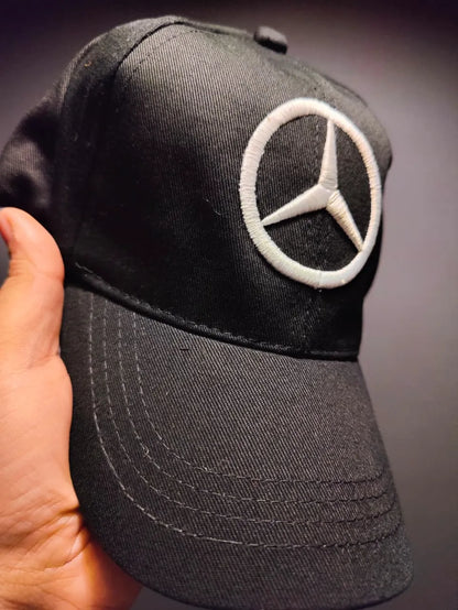 Black cap with Mercedes-Benz logo held by a hand against a dark background