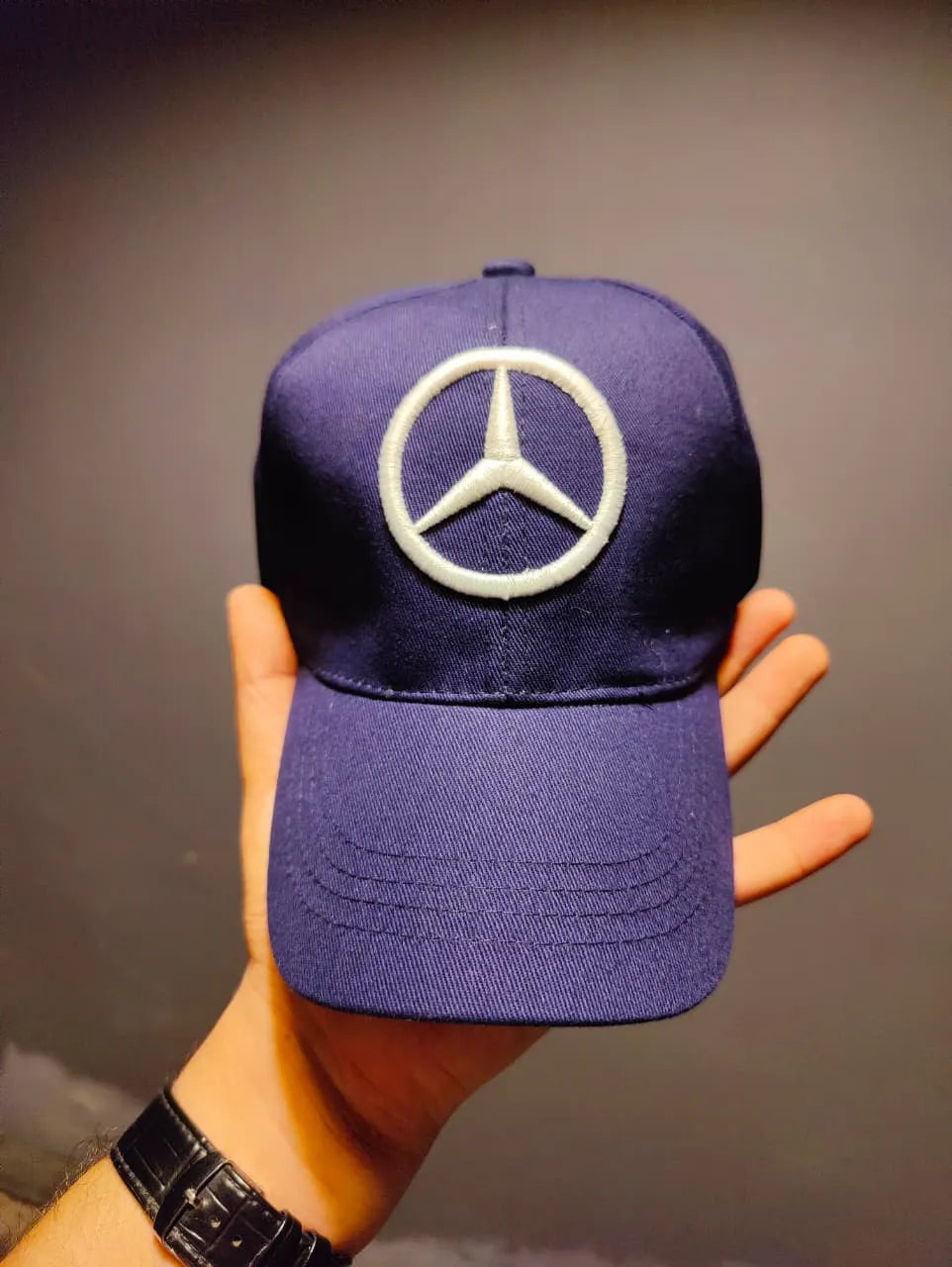 Purple cap with Mercedes-Benz logo held by a hand against a neutral background