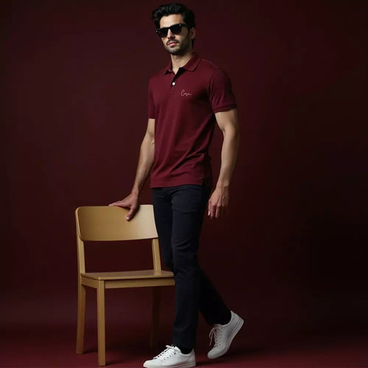 Man wearing a maroon polo shirt with a logo, black pants, and white sneakers against a dark red background.