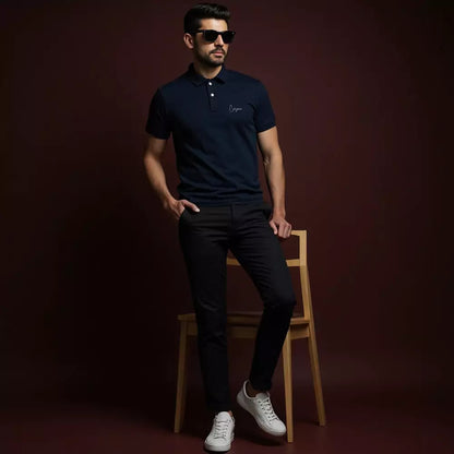 Man wearing a navy polo shirt with a logo, black pants, and white sneakers on a dark background