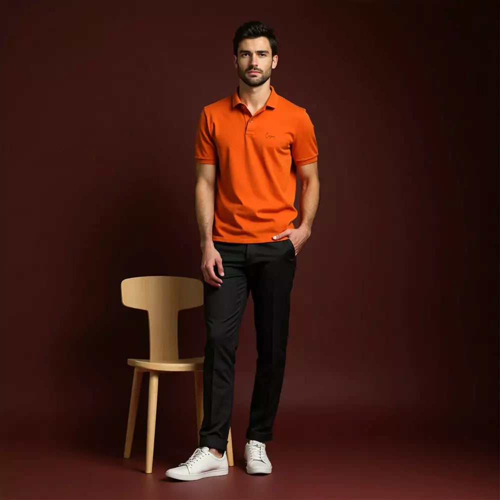 Man wearing an orange polo shirt and black pants standing next to a wooden chair on a dark red background