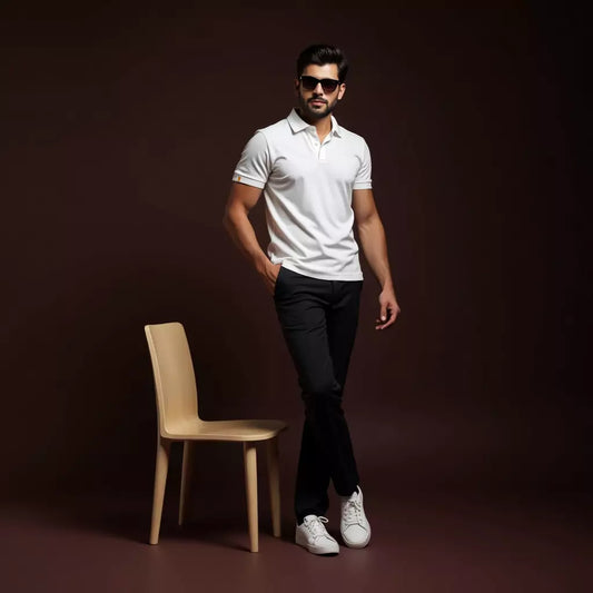 Man in white polo shirt and black pants standing next to a wooden chair on a dark background