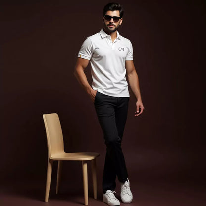 Man in a white polo shirt and black pants standing next to a wooden chair against a dark background